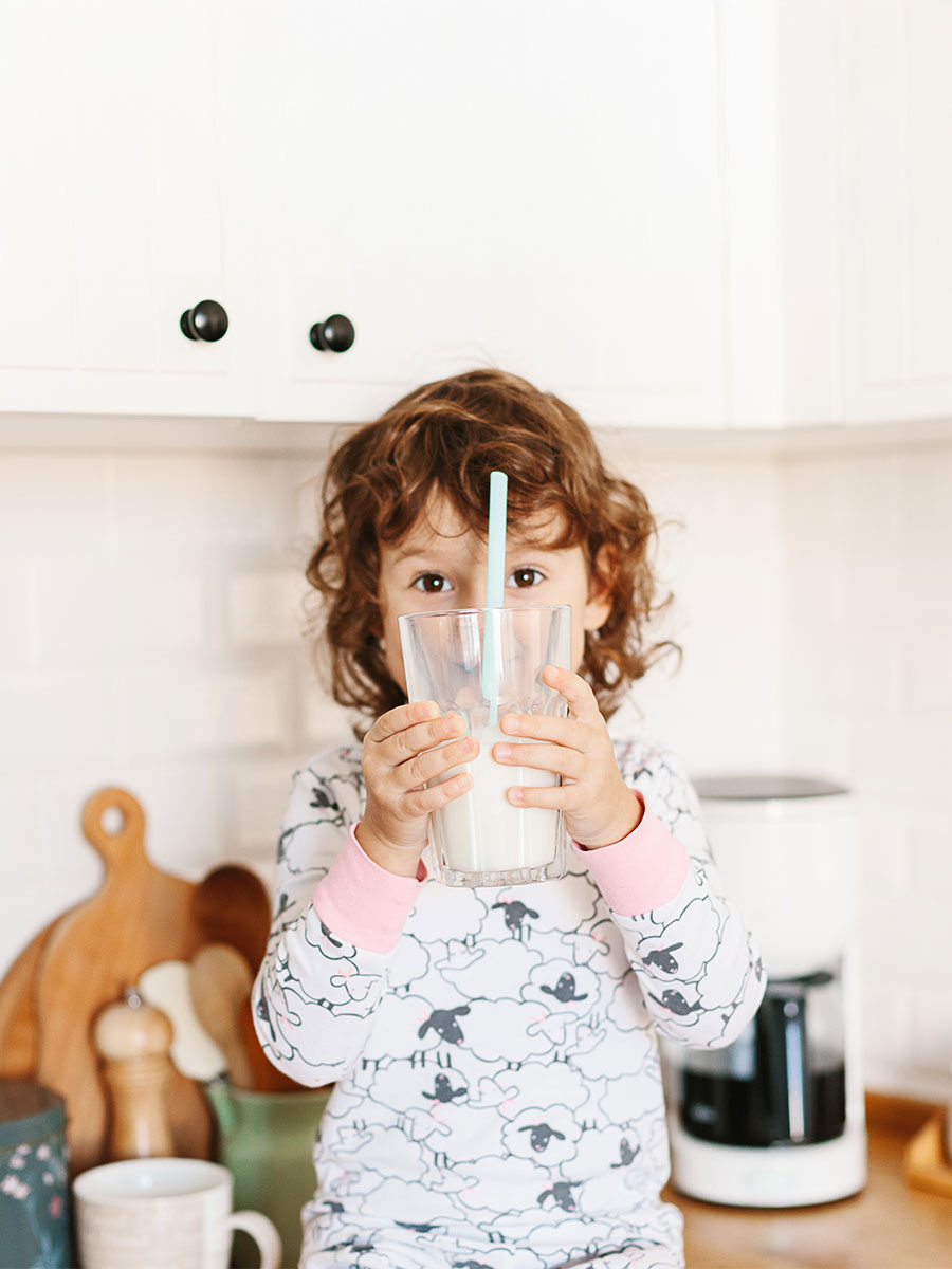 Little girl wearing pajamas drinking milk sitting on kitchen table in the morning. Foucs on hands holding glass of milk