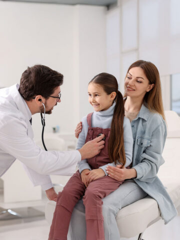 Little girl and her mother having appointment with pediatrician in hospital. Doctor checking child with stethoscope