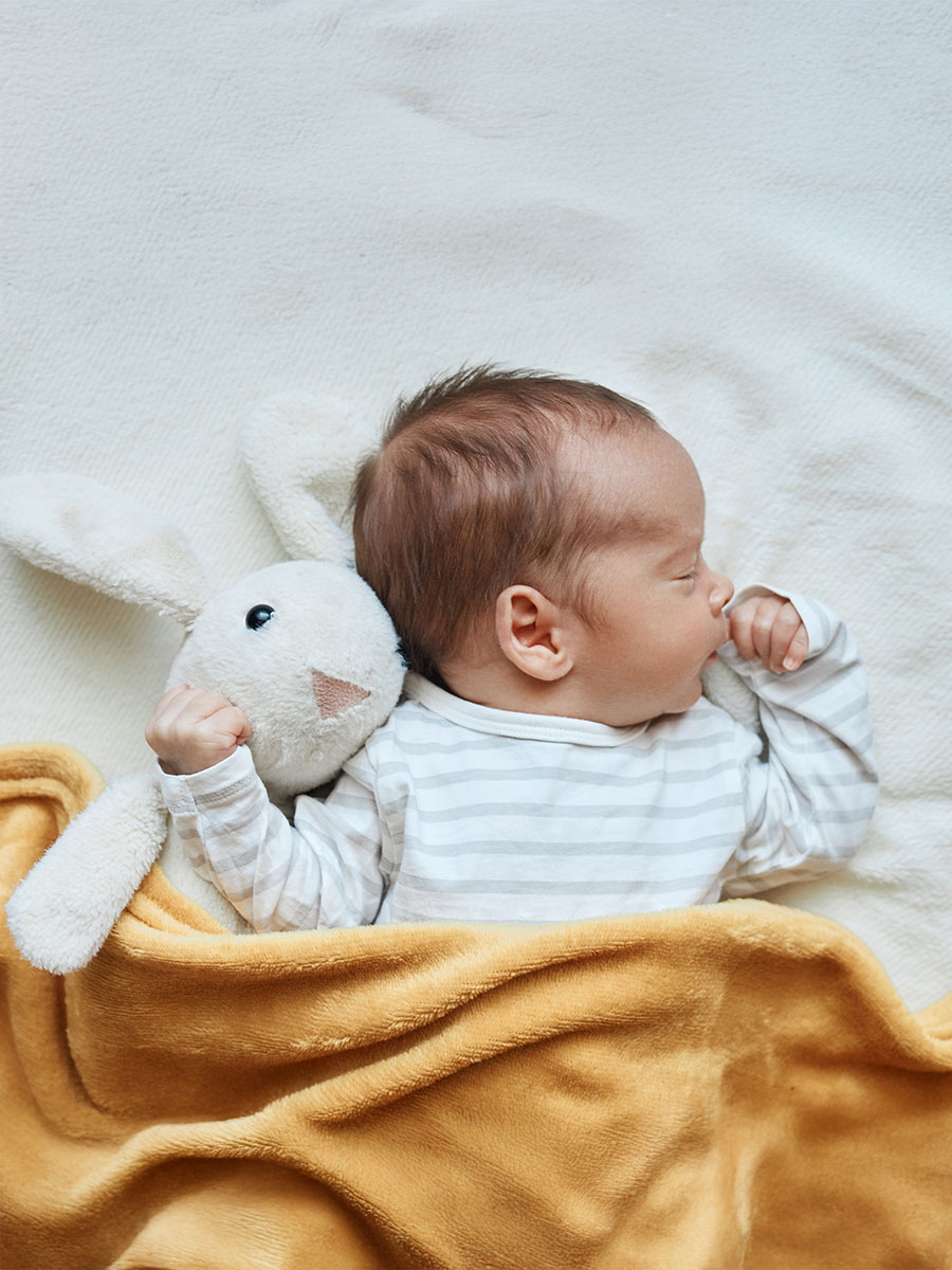 Newborn baby boy in bed sleeping under yellow soft blanket with fluffy rabbit toy comfortable bedding for kids infant child napping in bed